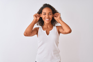 Young brazilian woman wearing casual t-shirt standing over isolated white background Smiling pulling ears with fingers, funny gesture. Audition problem