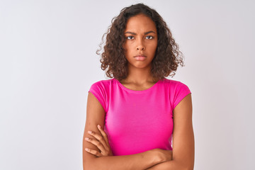 Young brazilian woman wearing pink t-shirt standing over isolated white background skeptic and nervous, disapproving expression on face with crossed arms. Negative person.