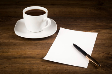 A cup of coffee, a sheet of paper with a pen on the counter from the desk