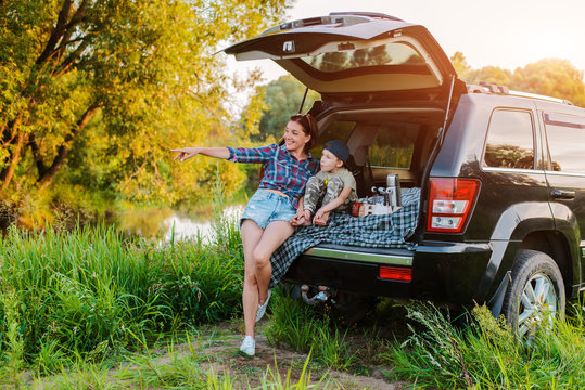 mother woman and child son comfortably relax in nature by the river sitting on the trunk of a jeep.