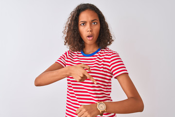 Young brazilian woman wearing red striped t-shirt standing over isolated white background In hurry pointing to watch time, impatience, upset and angry for deadline delay