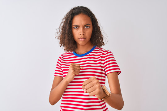 Young brazilian woman wearing red striped t-shirt standing over isolated white background Punching fist to fight, aggressive and angry attack, threat and violence