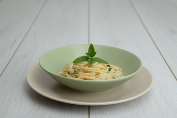 dish of spaghetti with spring onion and mint in an elegant wooden table