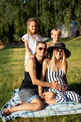 Picture of father and pregnant mother with children sitting on plaid on picnic on summer day