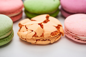 close up view of colorful French macaroons of different flavors with smashed one on white background