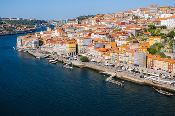 Fototapeta na wymiar River Douro with embankment of Porto and boats. Porto panoramic landmark on sunny day. Old buildings with brick roofs by river Douro in Porto, Portugal. Historic district of Porto. Portuguese vacation