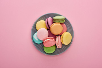 top view of multicolored delicious French macaroons on plate on pink background