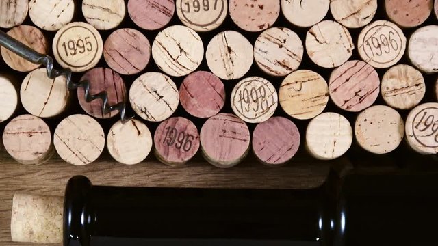 A large group of used wine corks in rows with a bottle and corkscrew