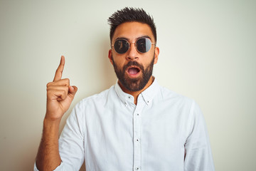 Fototapeta na wymiar Handsome indian buinessman wearing shirt and sunglasses over isolated white background pointing finger up with successful idea. Exited and happy. Number one.