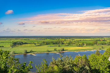 Fototapeta na wymiar View over the Elbauen in Lower Saxony, Germany. You see a landscape with fields, meadows and the river Elbe under a blue sky with clouds, which are illuminated by the sun.