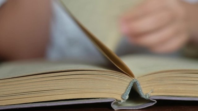 panoramic shot close-up of the expanded book lying on the Desk. The student reads and flips through the pages of the textbook.