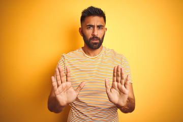 Young indian man wearing t-shirt standing over isolated yellow background Moving away hands palms...