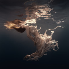 Girl in a dress with ribbons swims underwater