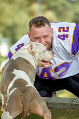 American football player with a dog posing on camera in a park. Copy space, sports banner. Concept american football, sport for the protection of animals.