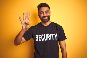 Arab indian hispanic safeguard man wearing security uniform over isolated yellow background showing and pointing up with fingers number four while smiling confident and happy.