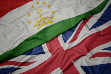 waving colorful flag of great britain and national flag of tajikistan.