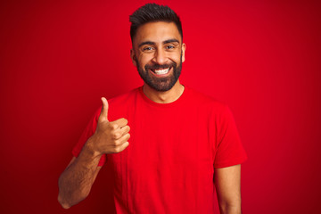 Young handsome indian man wearing t-shirt over isolated red background doing happy thumbs up...