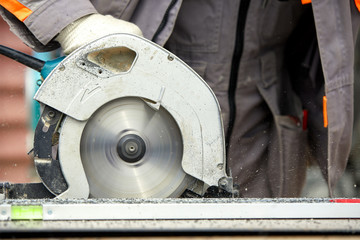 A construction contractor worker using a worm-driven hand-held circular saw to cut boards and...