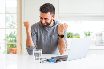 Handsome hispanic man working using computer laptop very happy and excited doing winner gesture with arms raised, smiling and screaming for success. Celebration concept.