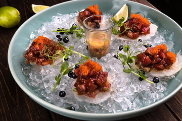 Closeup Red tuna tartare in ice on the green plate with lime and blueberries. Wooden brown background