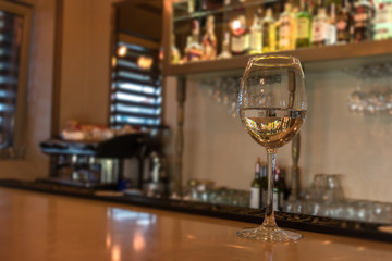 Glass of wine on bar counter in pub or restaurant. Bright blurred background with a coffee machine and glasses. Space for text