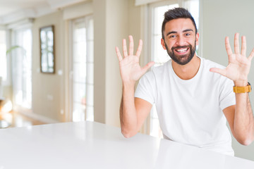 Handsome hispanic man casual white t-shirt at home showing and pointing up with fingers number ten while smiling confident and happy.