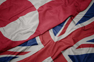 waving colorful flag of great britain and national flag of greenland.