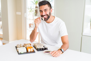 Handsome man smiling happy enjoying eating fresh colorful asian sushi using chopsticks