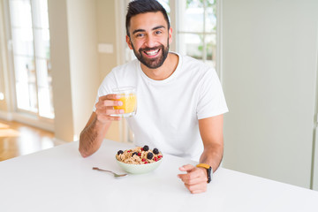 Handsome man smiling eating healthy breakfast and drinking orange juice in the morning