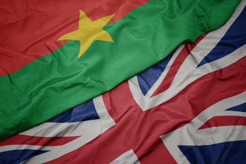 waving colorful flag of great britain and national flag of burkina faso.