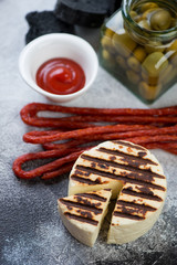 Close-up of whole grilled cheese, smoked meats and olives over light-grey stone background, vertical shot