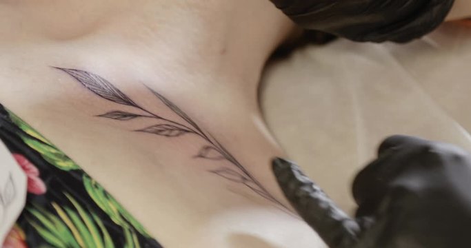 Drawing needle with ink. Tattoo master is painting details of picture drawing leaves nature pattern body art image on client skin, hands closeup. She is using professional tattoo machine in studio.
