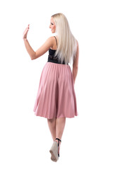Back view of elegant stylish blonde woman walking away looking at someone and waving hand. Full body isolated on white background. 
