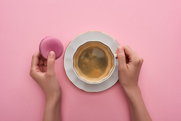 cropped view of woman drinking coffee with delicious French macaroon on pink background