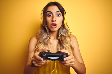 Young beautiful woman playing video game using gamepad over yellow isolated background scared in shock with a surprise face, afraid and excited with fear expression © Krakenimages.com
