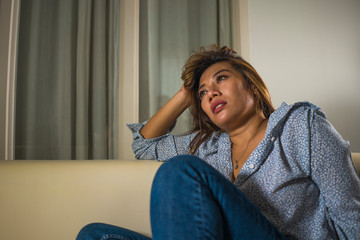 young beautiful sad and depressed woman thoughtful and confused at home couch feeling broken heart...