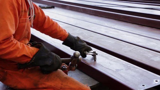 Trabajador martillando una barra de acero con guantes y uniforme naranja