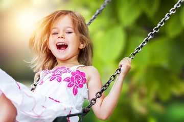 Little child blond girl having fun on a swing