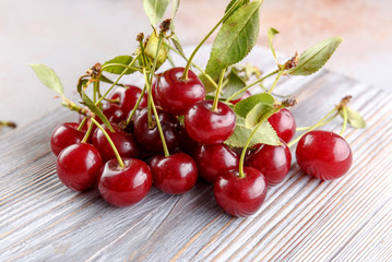 Fresh sweet cherries bowl with leaves on stone background, top view
