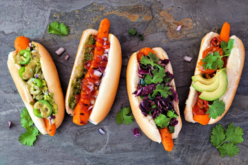Carrot vegan hot dogs with assorted toppings. Above view scene on a dark slate background. Plant...