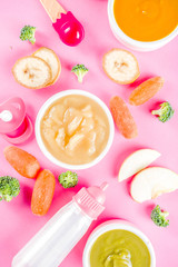Infant baby food concept. Bowls with vegetable fruit puree, green, orange, yellow colors - broccoli, carrots, banana, apple. With baby accessories and toys pink background Flat lay top view copy space