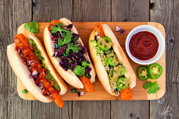 Carrot vegan hot dogs with assorted toppings. Top view on serving board with a rustic wood...