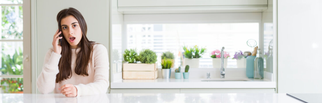 Wide angle picture of beautiful young woman having a conversation on smartphone scared in shock with a surprise face, afraid and excited with fear expression