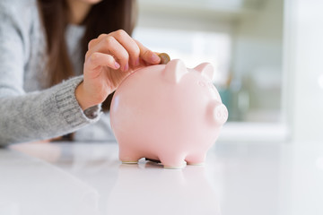 Young woman putting a coin inside piggy bank as savings for investment