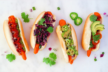 Carrot hot dogs with assorted toppings. Top view on a white marble background. Plant based meatless meal concept.
