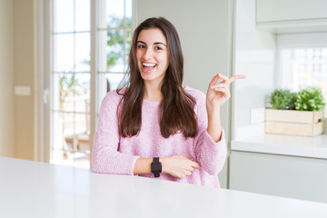 Beautiful young woman wearing pink sweater with a big smile on face, pointing with hand and finger to the side looking at the camera.