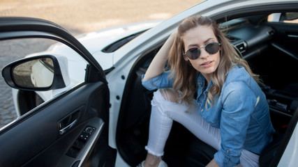 Happy young blonde woman sitting in a white car. Portrait of a successful attractive woman