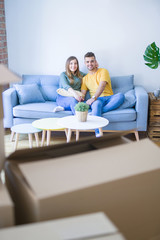 Young beautiful couple sitting and hugging on the sofa at new apartment with cardboard boxes around them, very excited for moving to a new home