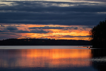 Fototapeta na wymiar Sunset at lake Saimaa at Finland. Vivid colors. Captured through a tree and leafs in the foreground