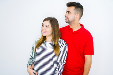 Fototapeta premium Young beautiful couple together over white isolated background looking away to side with smile on face, natural expression. Laughing confident.